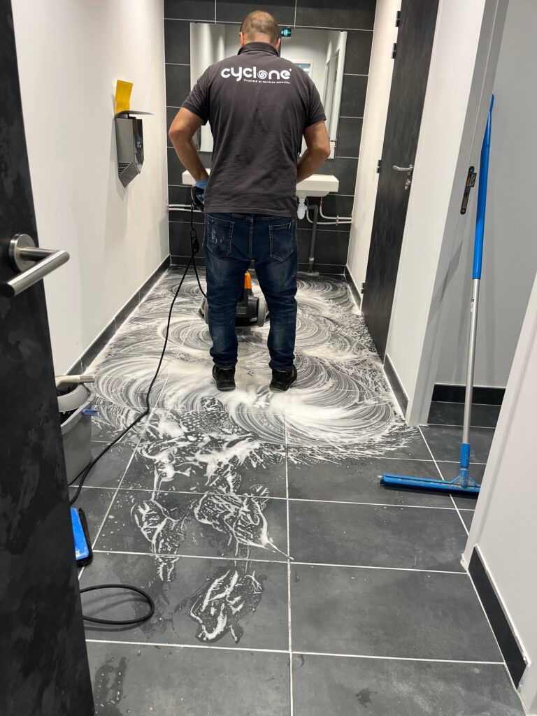 Agent Cyclone utilisant une monobrosse pour le nettoyage d'un sol carrelé avec mousse savonneuse.