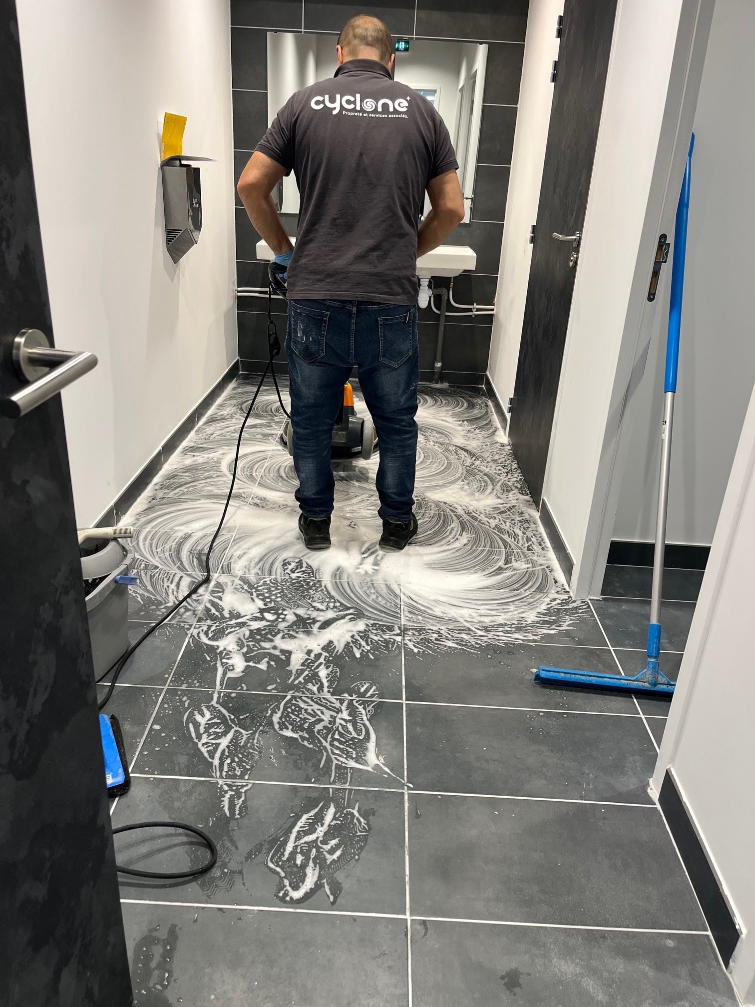 Décapage de Sol Agent Cyclone utilisant une monobrosse pour le nettoyage d'un sol carrelé avec mousse savonneuse.